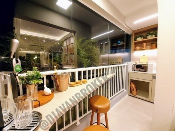 Varando do apartamento de 43m². A varanda está fechada por vidro e possui uma churrasqueira a carvão ecológica, guarda corpo de aço, no lado esquerdo tem dois bancos e sobre estes bancos consta uma mesa com vasos e uma chopeira Heineken.